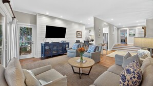 A spacious living room with a flat-screen TV, comfortable seating, and a view of the kitchen.