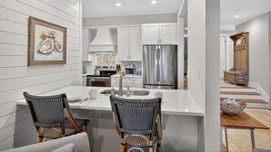 A modern kitchen with white cabinetry, stainless steel appliances, and a dining area with two wicker chairs.