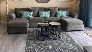 A living room with a sectional sofa, two side tables, a decorative mirror, and artwork on the walls. - Beautiful Condo On The Gulf, Walking Distance to Pier Park (Panama City Beach)