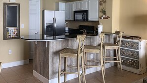 A modern kitchen with white cabinets, a black refrigerator, a microwave, and a wooden island with bar stools. - Beautiful Condo On The Gulf, Walking Distance to Pier Park (Panama City Beach)