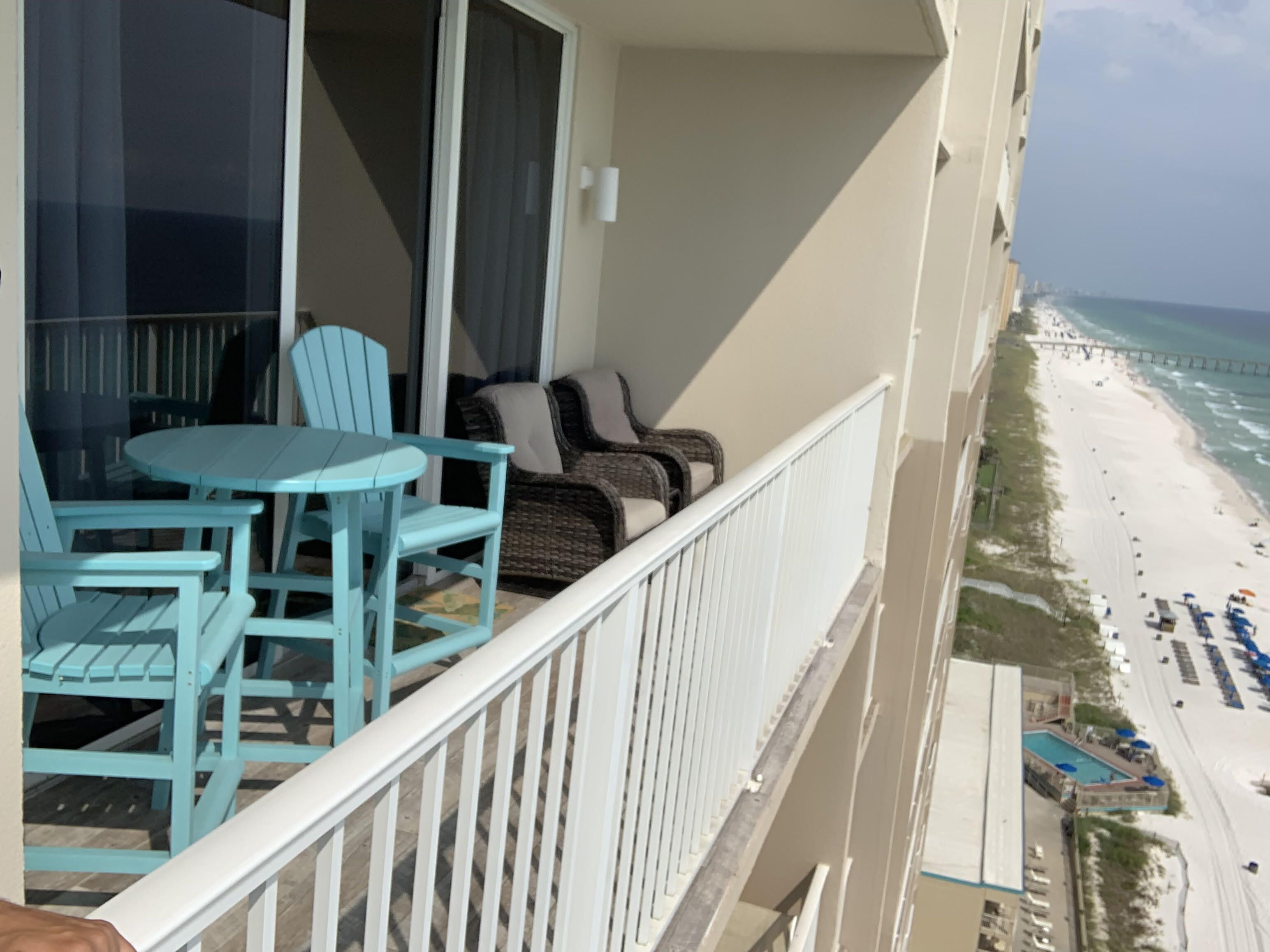 Un balcon avec une table et des chaises, donnant sur une plage avec une jetée et un espace piscine.