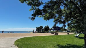 A beach with a wooden boardwalk, grassy areas, and a large house in the background. - Steps to beach! Custom-built house with panoramic ocean views, wrap-around deck. (Guilford Center)
