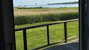 A view from a room with a wooden deck overlooking a grassy area and a body of water. - Steps to beach! Custom-built house with panoramic ocean views, wrap-around deck. (Guilford Center)