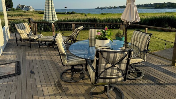 A deck with outdoor furniture, a glass table, and a view of the water. - Steps to beach! Custom-built house with panoramic ocean views, wrap-around deck. (Guilford Center)