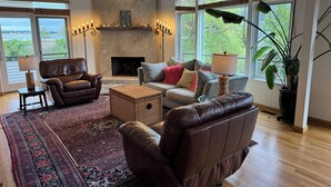 A spacious living room with a fireplace, leather sofas, a large rug, and large windows with views of greenery. - Steps to beach! Custom-built house with panoramic ocean views, wrap-around deck. (Guilford Center)