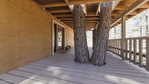 Una terraza cubierta de madera con dos árboles grandes en el centro, baranda de madera en un lado y puerta que da a un espacio al aire libre.