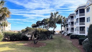 A residential area with a well-maintained lawn, palm trees, and a row of two-story houses with balconies. - Port O' Call D101 by Deserving Vacations (Isle of Palms)