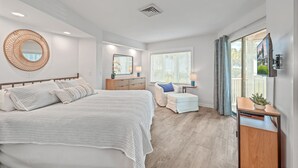 A modern bedroom with a bed, bedside table, and a large window with curtains. - Port O' Call D101 by Deserving Vacations (Isle of Palms)