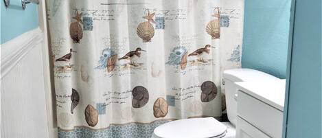 A bathroom with a shower curtain featuring bird and shell designs, a toilet, and a sink.