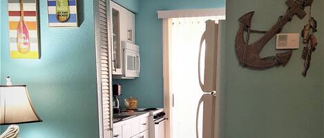 A kitchen with white cabinets, a microwave, and a stove. There is a door leading to another room.