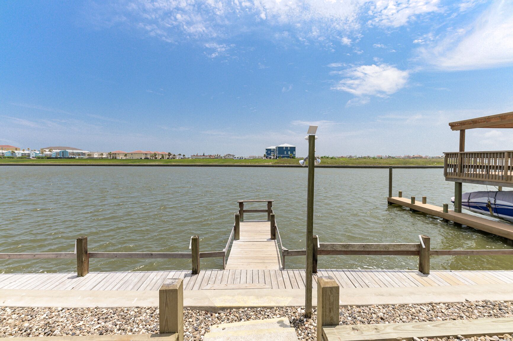 Eine Holzstege ragt in ruhiges Wasser hinein, über ihm ein klarer Himmel und am Horizont ein entferntes Gebäude.
