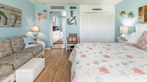 Un dormitorio con cama, sofá, mesita de noche y cómoda. Hay una puerta que da a un baño.