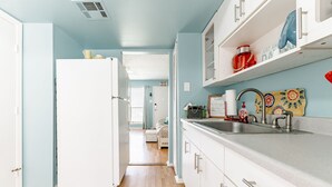 Una cocina con un refrigerador blanco, un lavamanos con dispensador de jabón rojo y una pared decorativa con un letrero que dice 'Peach'.
