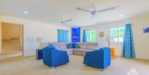 A spacious living room with a beige sectional sofa, two blue armchairs, a ceiling fan, and a staircase leading to another level. - Beautiful private gated 2 bedroom home with  pool, terraces and ample parking. (Isla Mujeres)