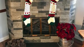 A fireplace with a stone mantle, decorated with Christmas stockings, a snowman, and poinsettias.
