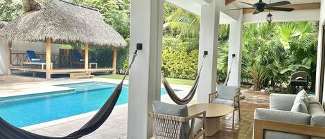 A poolside area with a hammock, seating, and a view of the pool and surrounding greenery.