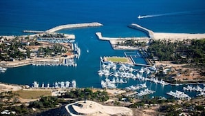 Une vue aérienne d’une marina avec de nombreux quais et des bateaux, entourée de zones résidentielles et d’une plage de sable.