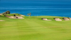Un parcours de golf avec des bunkers et un mât de drapeau, offrant une vue sur l’océan.