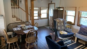 Un coin repas avec une table et des chaises en bois, un fauteuil à motifs et un escalier.