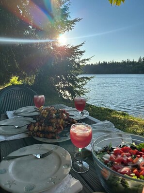 En matplats vid sjön med grill, sallad och dryck.