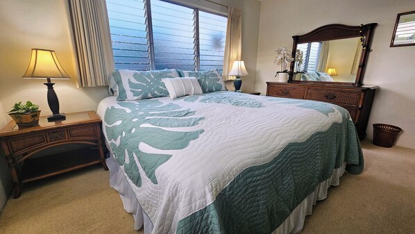 Un dormitorio con cama, mesitas de noche, cómoda, espejo y ventana con persianas.