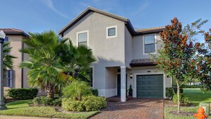 A two-story house with a brick driveway, a green garage door, and a palm tree in the front yard. - Spacious 6BR Family Retreat w/ Private Pool and Spa in Resort Community! (Davenport)