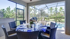 An outdoor dining area with wicker chairs and a glass table set for a meal, overlooking a swimming pool and greenery. - Spacious 6BR Family Retreat w/ Private Pool and Spa in Resort Community! (Davenport)