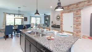 A modern kitchen with granite countertops, a central island, and pendant lighting. - Spacious 6BR Family Retreat w/ Private Pool and Spa in Resort Community! (Davenport)