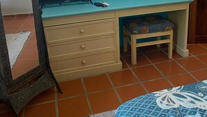 Een slaapkamer met een bed, een bureau met stoel, een dressoir, een spiegel en een plafondventilator.
