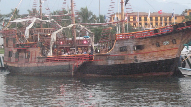 Een groot, klassiek schip afgemeerd in een haven met een bergachtig landschap op de achtergrond.