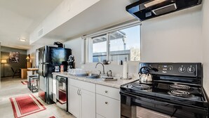Uma cozinha moderna com fogão preto, armários brancos e janela com vista para uma varanda.