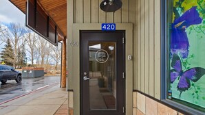 A building entrance with a number sign '420' above the door, a glass door with a reflection, and a large window with a purple flower design. - Spacious Luxury Downtown Riverfront Loft Condo.  License #6027 (Estes Park)