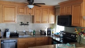 A kitchen with wooden cabinets, a microwave, a stove, and a sink. - Maui Rainbows And Waves!~Gorgeous Oceanfront Views!! ~ 2 Bdrm ~Corner unit w A/C (Lahaina)