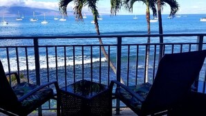 A balcony with two chairs facing a beach with sailboats and palm trees. - Maui Rainbows And Waves!~Gorgeous Oceanfront Views!! ~ 2 Bdrm ~Corner unit w A/C (Lahaina)