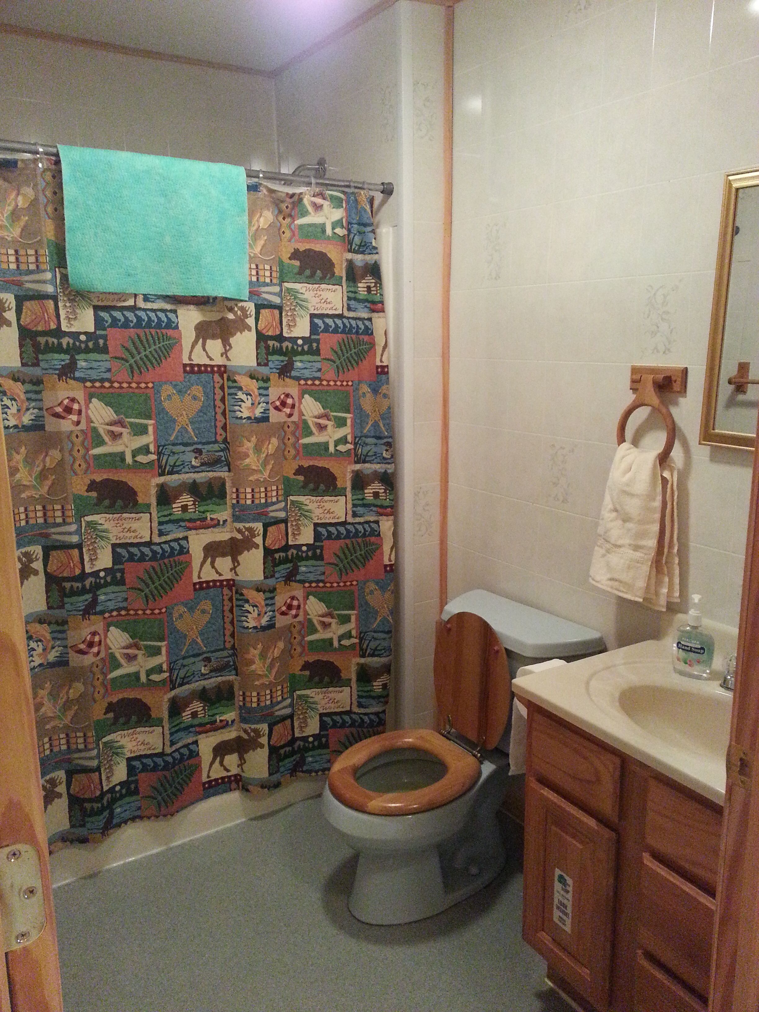 Un baño con inodoro de madera, un lavabo con espejo y una cortina de ducha con diseño de vida silvestre.
