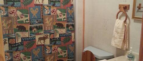 Un baño con inodoro de madera, un lavabo con espejo y una cortina de ducha con diseño de vida silvestre.