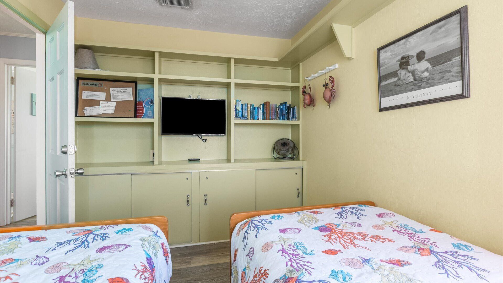 Une chambre avec deux lits, une télévision, une bibliothèque et un tableau encadré au mur.