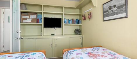 Une chambre avec deux lits, une télévision, une bibliothèque et un tableau encadré au mur.