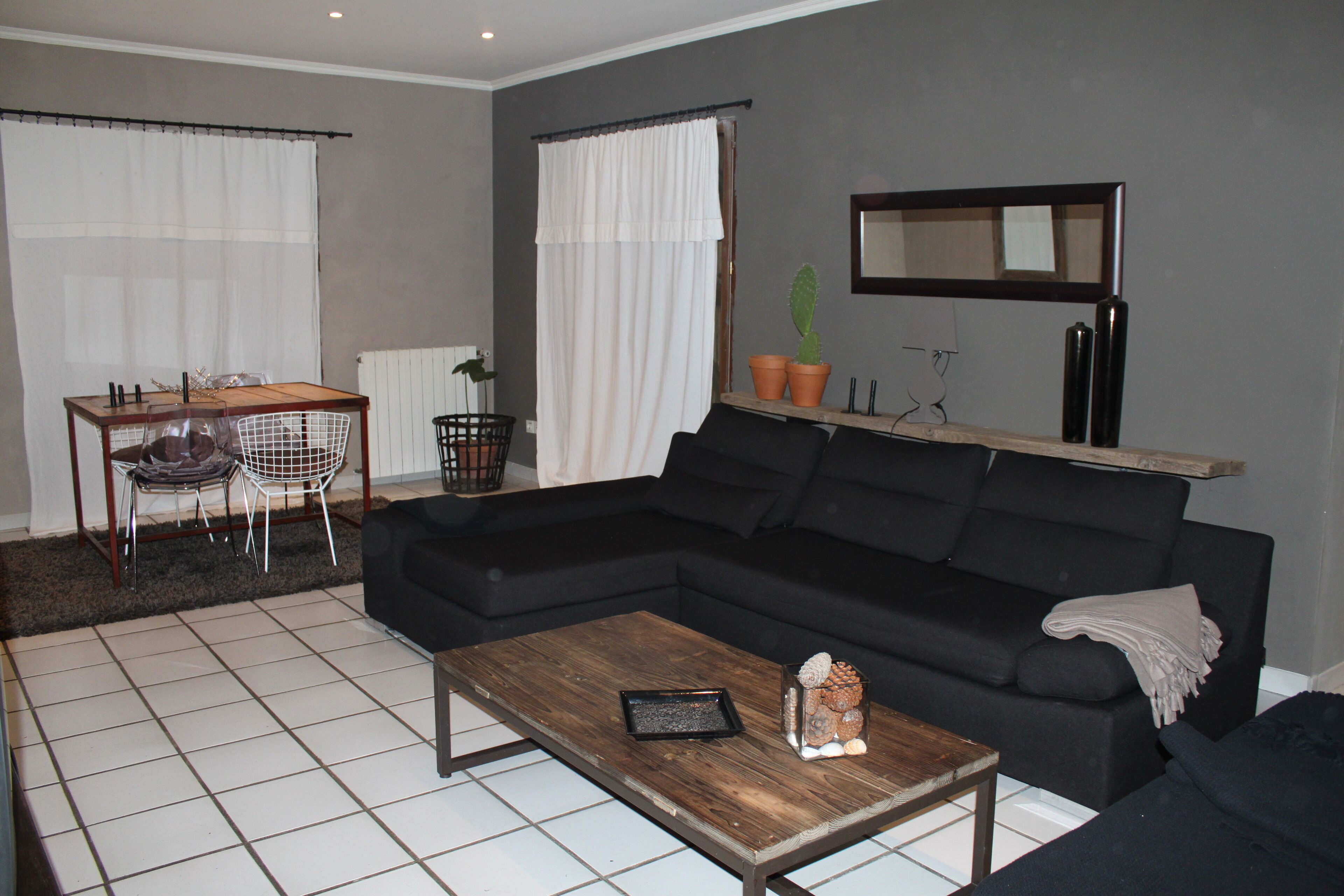 A living room with a black sofa, a wooden coffee table, a dining table with chairs, and a potted plant.