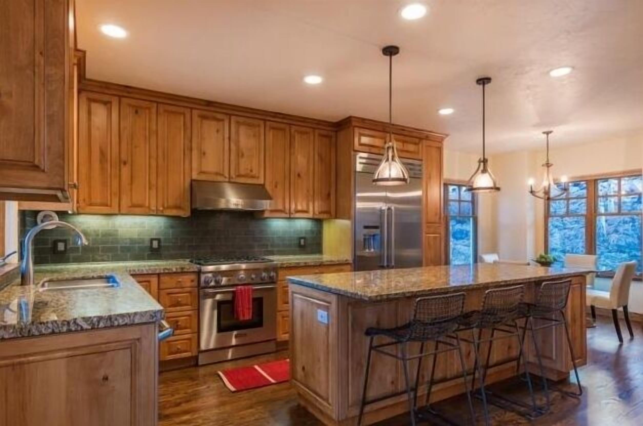 A kitchen with wooden cabinets, stainless steel appliances, granite countertops, and a bar area with stools.