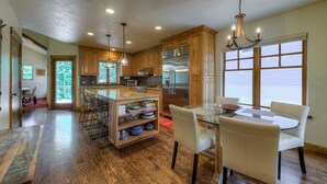 A spacious kitchen with wooden cabinets, a central island with seating, and a dining area with a glass table and chairs.