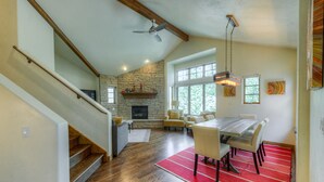 A spacious living area with a stone fireplace, a dining table, and a staircase.