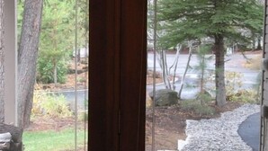 A view through a glass door leading to a paved outdoor area with a stone wall and a tree. - Family Friendly, Air Conditioning - SHARC passes included. (Sunriver)