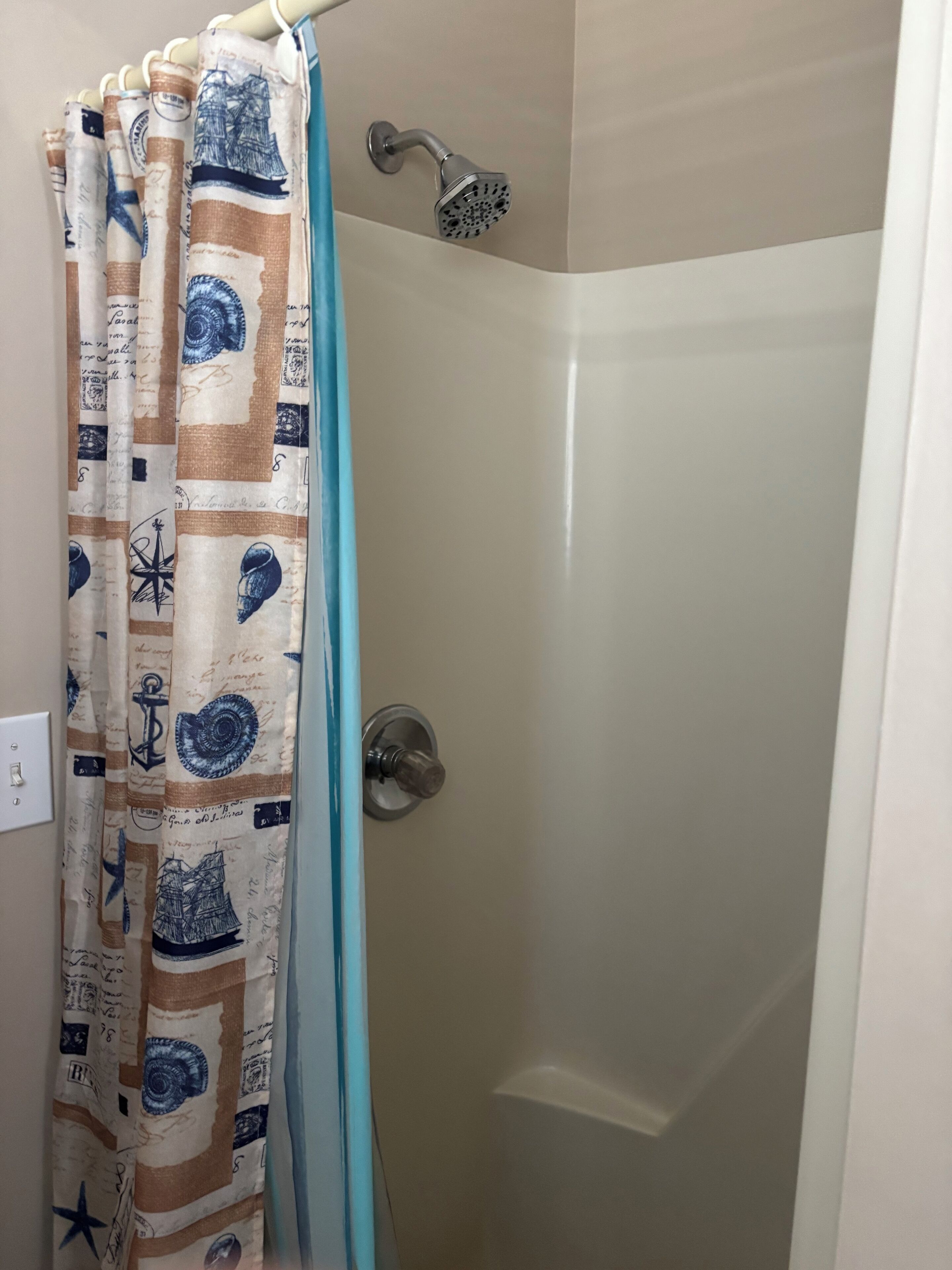 Un espace douche doté d’une porte en verre et d’un rideau orné de motifs marins.