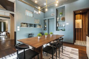 Un espace repas moderne avec une table en bois et des chaises noires, entouré d’étagères ornées d’objets décoratifs et de plantes.