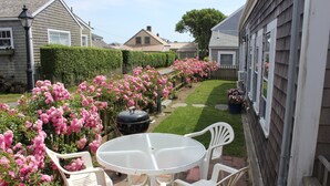 Een terras met een ronde tafel en vier stoelen, omringd door roze bloemen en een houten hek.