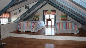 Een kamer met twee bedden, houten vloeren en een schuin plafond met zichtbare balken.