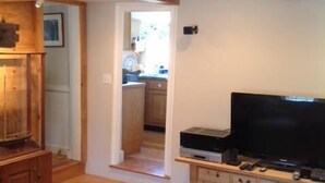 Een woonkamer met een houten vloer, een televisie en een houten kast. Een trap leidt naar een andere kamer.