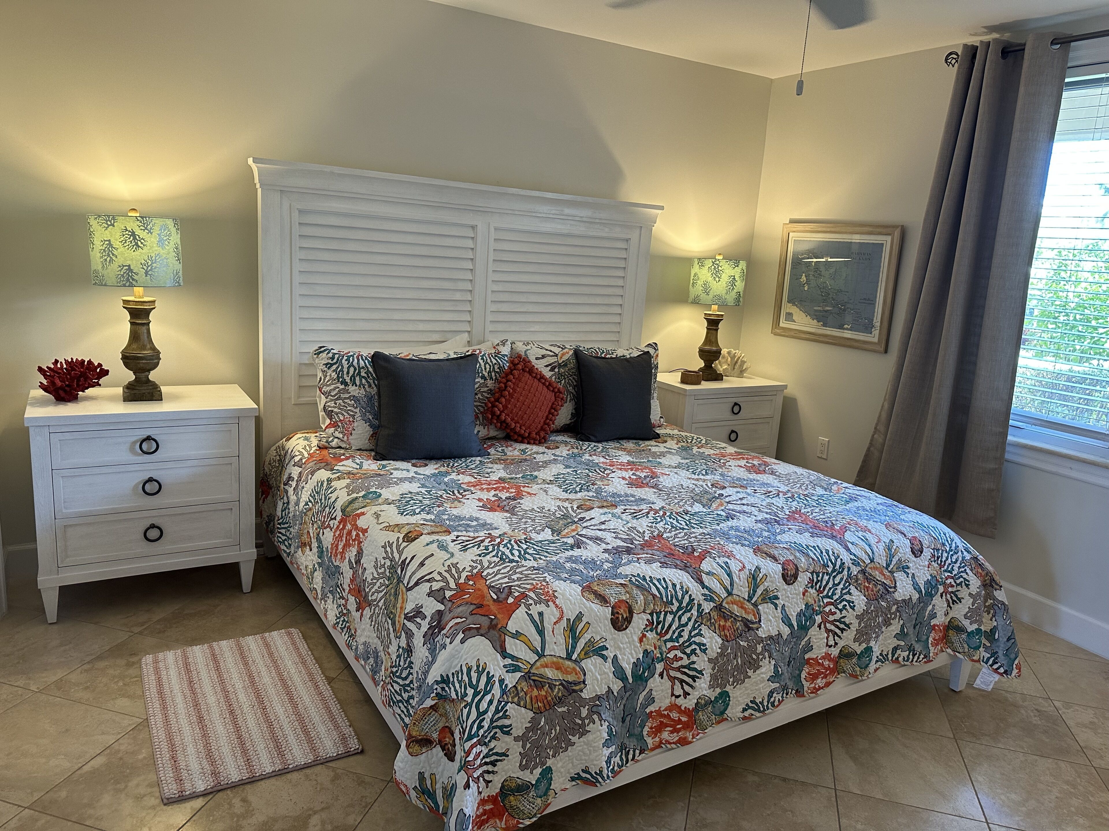 Une chambre à coucher avec un lit, des tables de chevet, une lampe, un tapis et une fenêtre avec des rideaux.