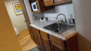 A kitchen with wooden cabinets, a granite countertop, a stainless steel sink, and a microwave. - Peaceful and Serene w/ Hot Tub and View (Eureka Springs)